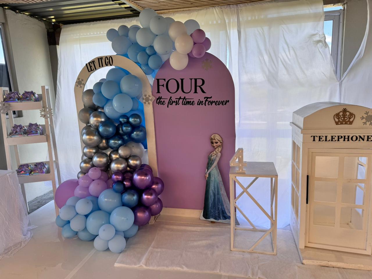 Frozen-themed backdrop with a pastel balloon garland, a “Let It Go” arch and a lilac FOUR panel
