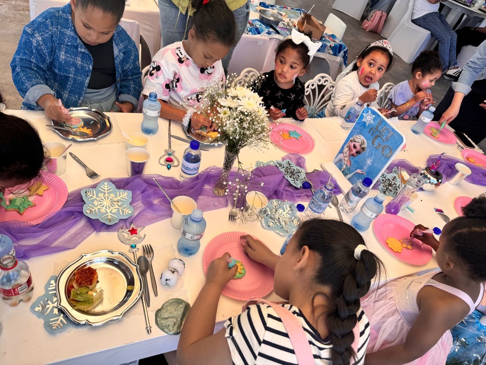 Kids decorating snowflake cookies and biscuits at the party table