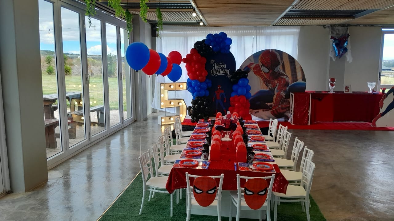 Spider-Man fifth birthday party table with red and blue balloon garlands and a light-up number five