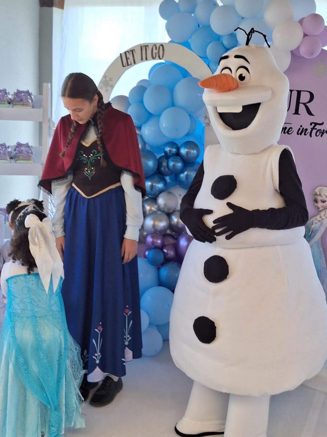 Anna and Olaf characters greeting party guests beside the Frozen balloon garland